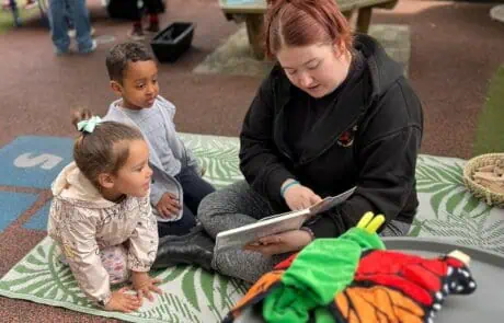 Staff reading children a book in outdoor area